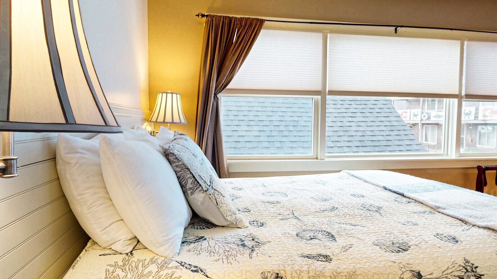 A bedroom with a bed, pillows, a lamp, and a window with blinds.