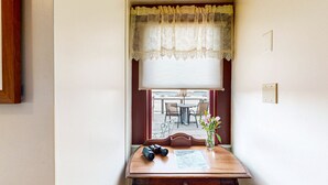 A room with a wooden table, a window with lace curtains, a vase with flowers, and a pair of binoculars. - The Roseway - Inn on the Harbor (Stonington)