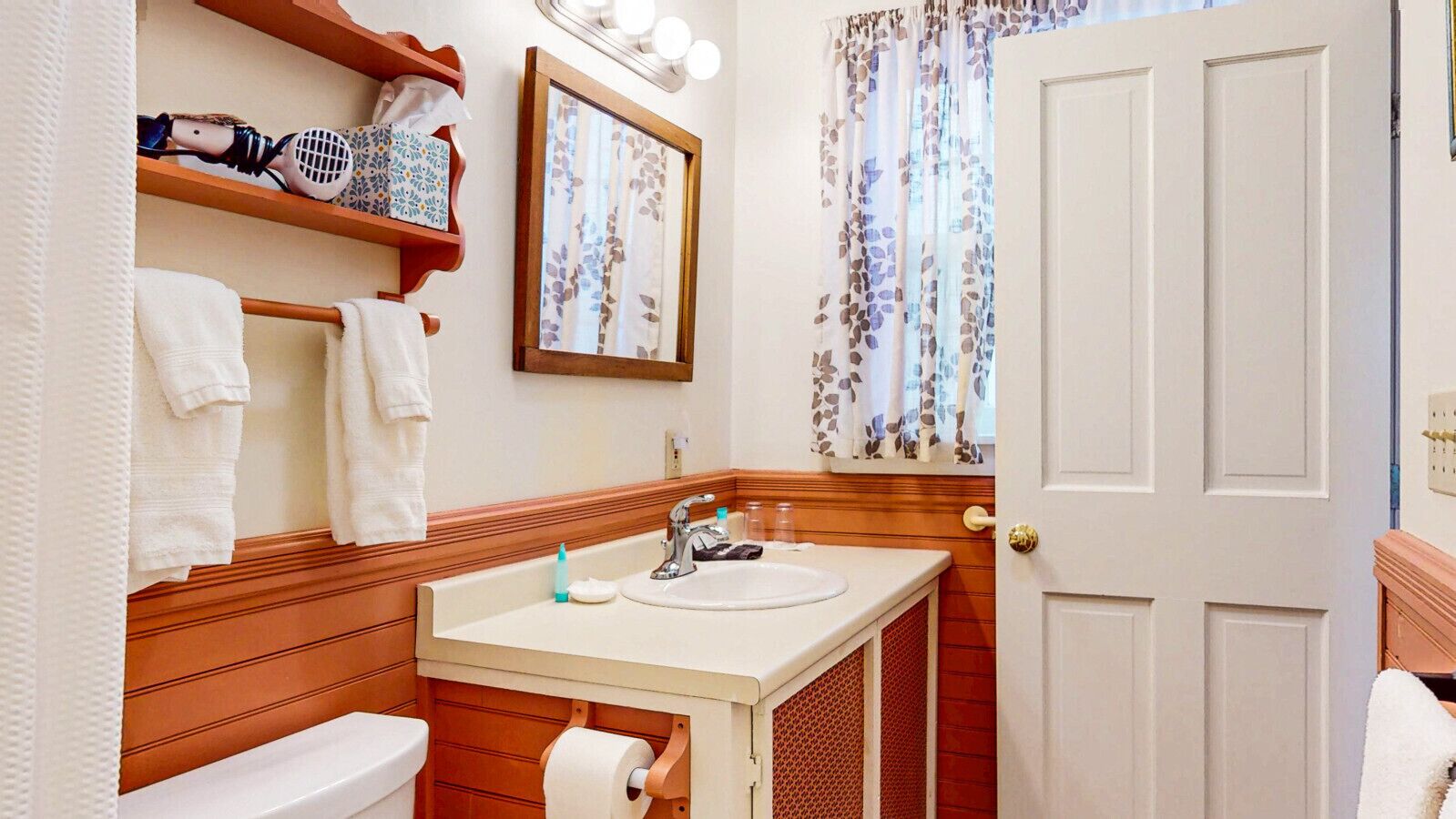 A bathroom with a wooden vanity, a white sink, a mirror, and a toilet.