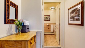 Un pasillo que conduce a un baño con un tocador de madera, un jarrón con flores y un cuadro en la pared.