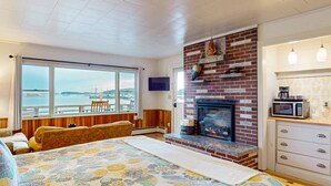 Una habitación con una cama grande, chimenea, vista al agua y kitchenette.