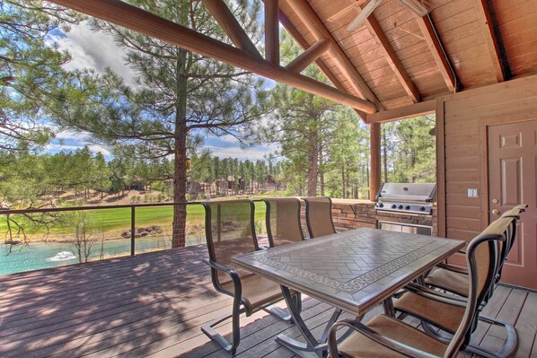 A covered outdoor patio with a table and chairs, a grill, and a view of a lake and forest. - Golf Course & Lake Views: Luxe Show Low Cabin (Show Low)