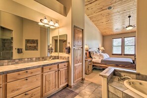 A spacious bathroom with a large vanity, a separate shower area, and a bedroom with a bed and nightstand. - Golf Course & Lake Views: Luxe Show Low Cabin (Show Low)