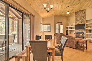 A spacious living area with a wooden ceiling, a fireplace, and a large window overlooking a deck. - Golf Course & Lake Views: Luxe Show Low Cabin (Show Low)