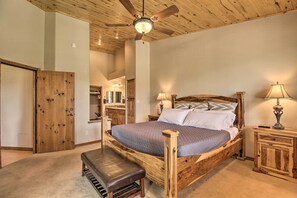 A bedroom with a wooden bed frame, a bench, a ceiling fan, and a nightstand with a lamp. - Golf Course & Lake Views: Luxe Show Low Cabin (Show Low)
