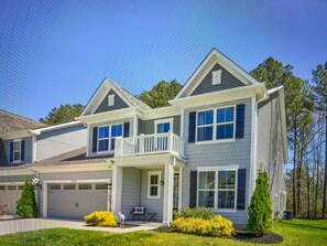 Stunning two-story home with a central entrance, covered porch, and seating area, set amidst beautifully manicured lawns and trees.