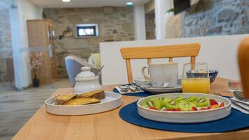 Una escena de desayuno con tostadas, fruta, una taza de café y un vaso de zumo de naranja sobre una mesa de madera.
