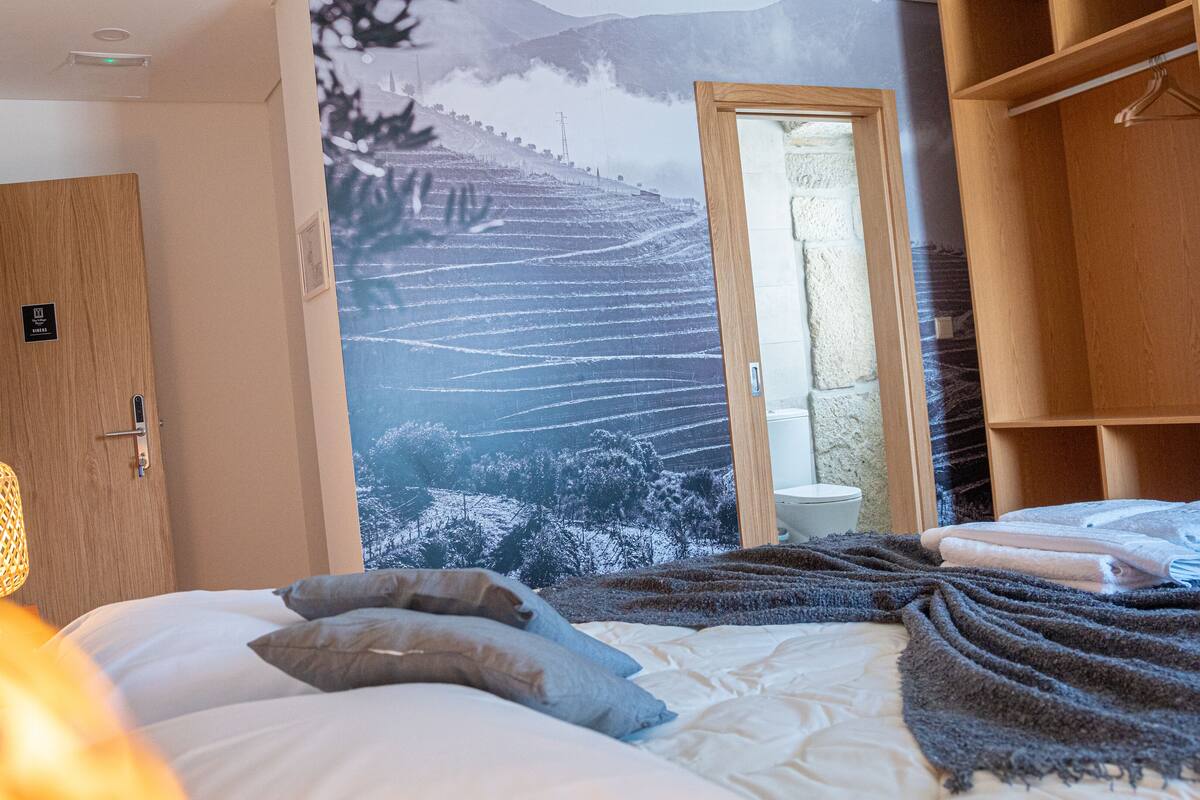 Ein Schlafzimmer mit Bett, Kissen, Decke, einem Holzschrank und einem durchgehenden Türbogen sichtbaren Badezimmer.