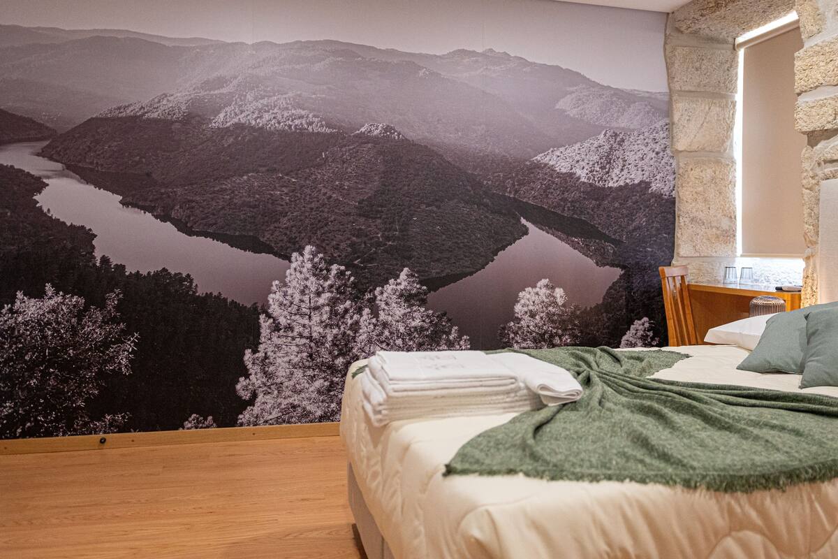 Ein Schlafzimmer mit Bett, Nachttisch, Spiegel und einer Wandmalerei einer Berglandschaft.