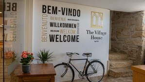 A reception area with a bicycle, a wooden bench, and a welcome sign in multiple languages. - The Village House by CDV (Carrazeda de Ansiaes)