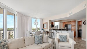 Ein modernes Wohnzimmer mit einer Couch und Sesseln, einem Essbereich und einer Küche mit Holzausstattung und Edelstahlgeräten.