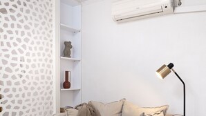 A modern living room with a beige sofa, a round black table with a yellow object, a floor lamp, and a white air conditioning unit on the wall. - Seaside Nestie by BluPine (Vari-Voula-Vouliagmeni)