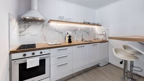 A modern kitchen with white cabinetry, a wooden countertop, a built-in oven, a stainless steel sink, and a bar stool. - Seaside Nestie by BluPine (Vari-Voula-Vouliagmeni)