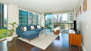 Una sala de estar moderna con un sofá azul, una mesa de centro de cristal y un mueble para televisor.