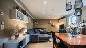 Ein modernes Wohnzimmer mit einer Couch, einem Esstisch und einer Küchenzeile im Hintergrund.