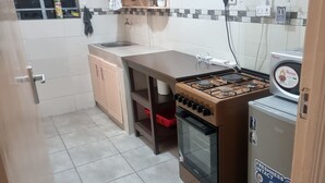 Een kleine keuken met een gasfornuis, een ingebouwde oven, een kleine koelkast en een spoelbak.