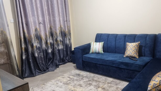 Een woonkamer met een blauwe bank, decoratieve kussens, een afstandsbediening en een siergordijn.
