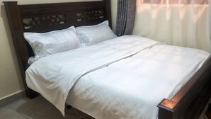Een keurig opgemaakt bed met een houten hoofdbord, wit beddengoed en een zichtbare stopcontact aan de zijkant.