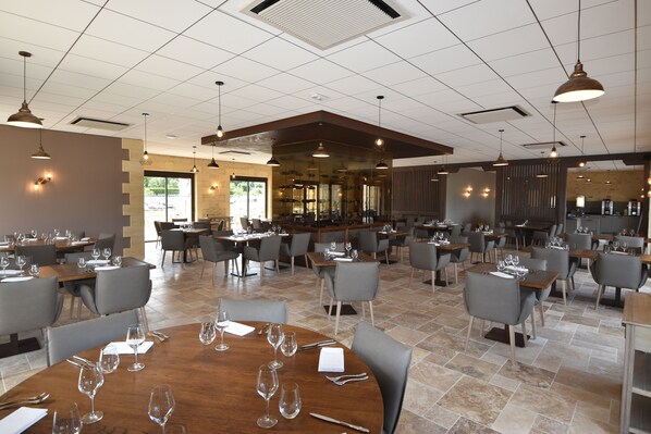 A spacious restaurant with multiple tables and chairs, a bar area, and a view of the outdoors. - Hotel le Périgord (La Roque-Gageac)