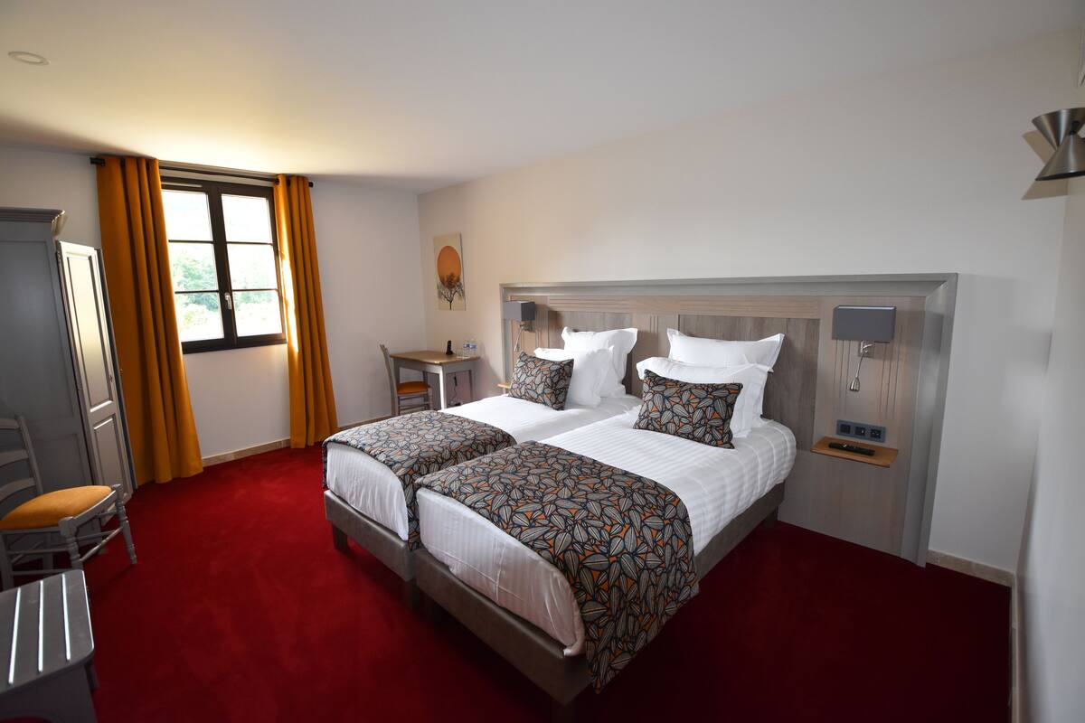 A hotel room with two beds, a desk, a chair, a wardrobe, and a window with curtains.