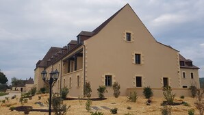 A large, beige building with a steep roof, multiple windows, and a small garden area with plants and a pathway. - Hotel le Périgord (La Roque-Gageac)