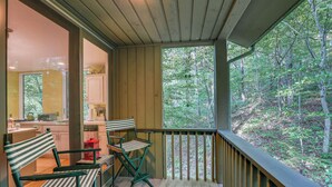 Eine Holzterrasse mit Geländer, einem Esstisch mit Stühlen und Blick auf einen Wald.
