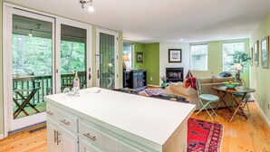Eine geräumige Küche mit einer großen Kochinsel, ein Essbereich mit Tisch und Stühlen, ein Wohnzimmer mit Sofa und Kamin sowie große Fenster mit Blick ins Grüne.