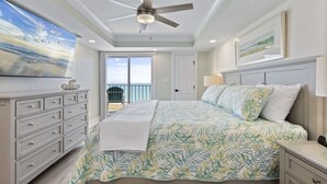 Une chambre avec un lit, un ventilateur de plafond, une télévision, une commode et un balcon avec vue sur l’océan.