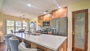 A modern kitchen with wooden cabinets, stainless steel appliances, a large island with bar stools, and a pantry door. - Sea Trail Resort Villas Condo w/ Community Perks! (Sunset Beach)