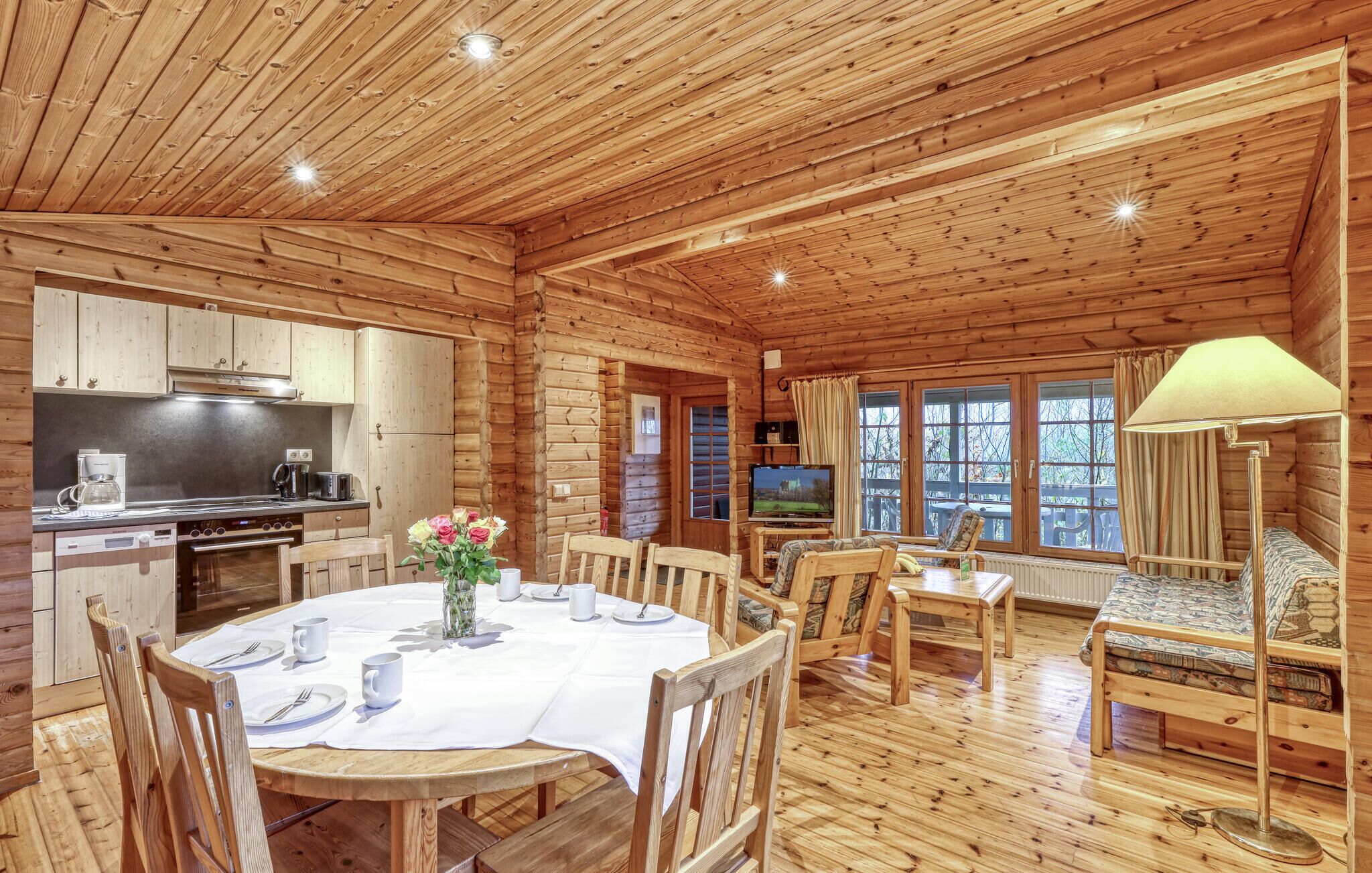 A wooden cabin interior with a dining area, kitchen, and a TV.