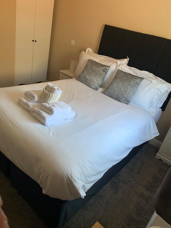A neatly made bed with white linens, two pillows with a woven pattern, and a folded towel on the bed.