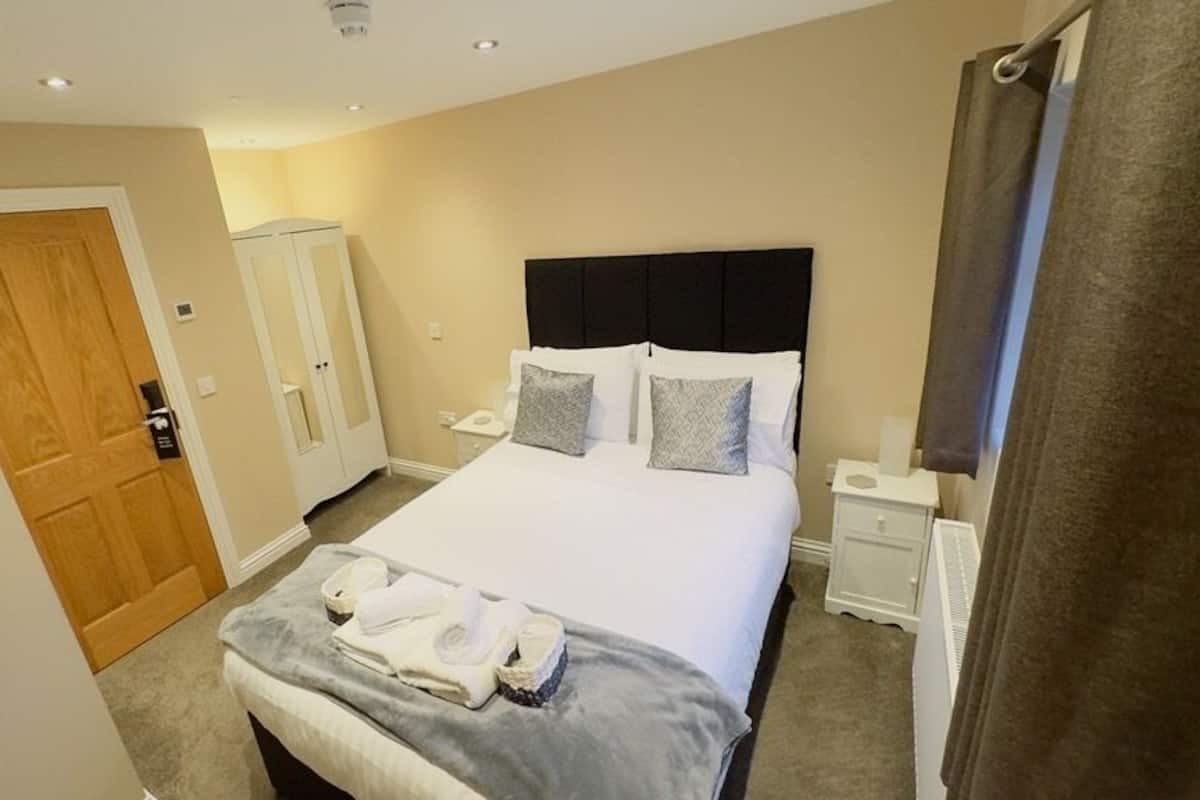 Habitación de hotel con una cama grande, una mesita de noche, un armario y una puerta.