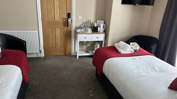 A hotel room with two beds, a desk with a chair, a television, and a radiator.