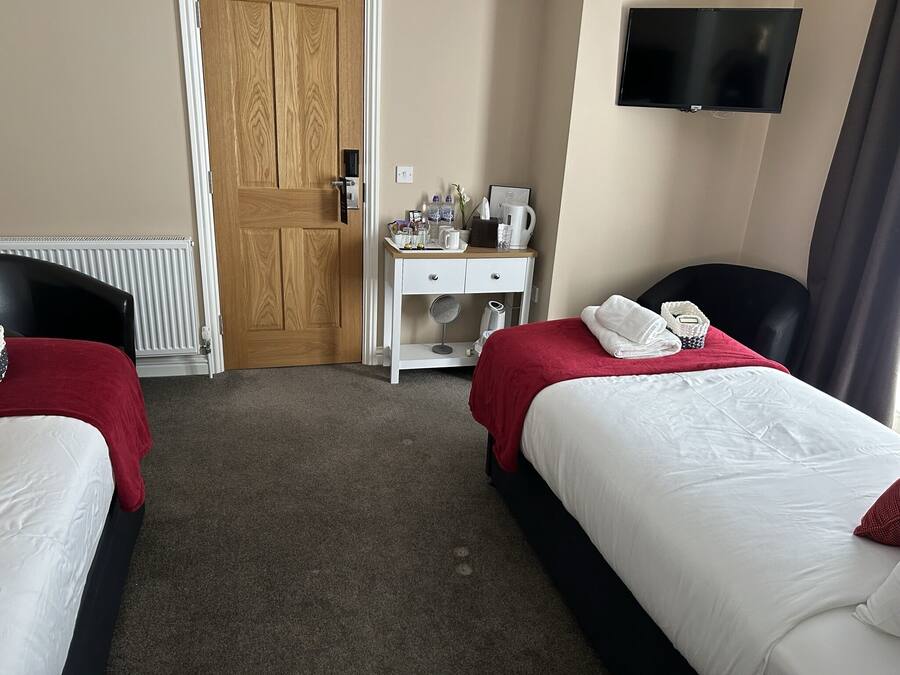 A hotel room with two beds, a desk with a chair, a television, and a radiator.