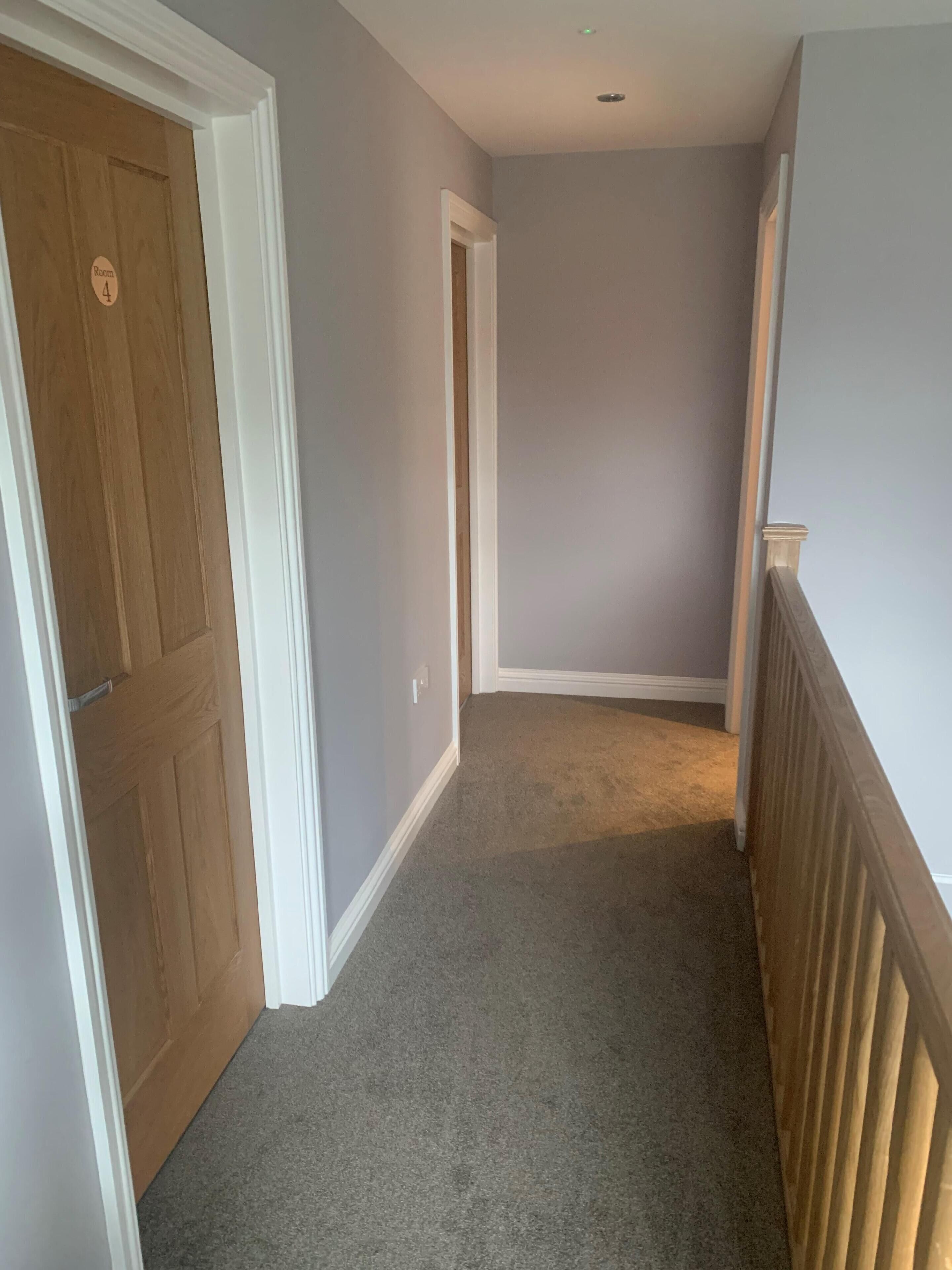 A narrow hallway with carpeted floors, white trim, and a wooden door labeled "Room 4".