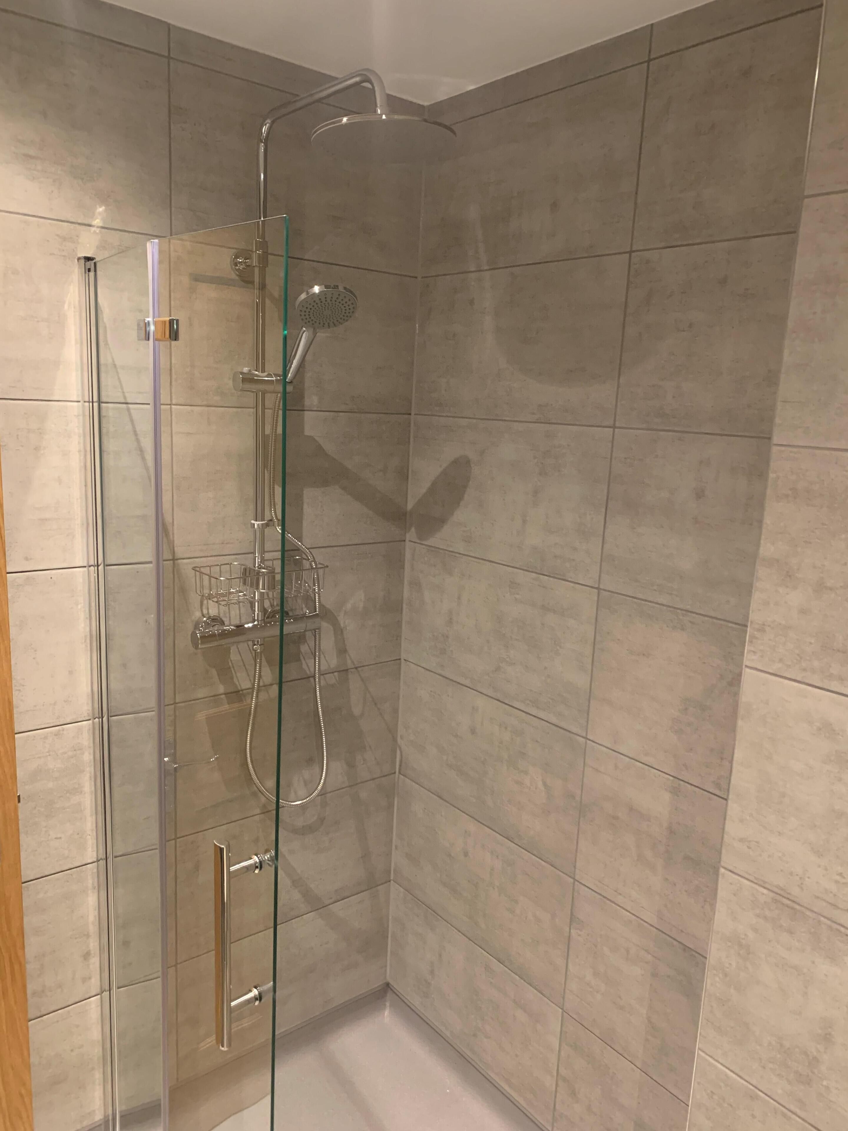 A glass-enclosed shower with a handheld showerhead and a handheld shower head.