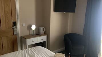 A hotel room with a bed, a desk with a lamp, a chair, a TV mounted on the wall, and a door.