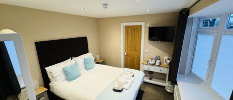 A hotel room with a bed, a bedside table with a lamp, a TV mounted on the wall, and a window.