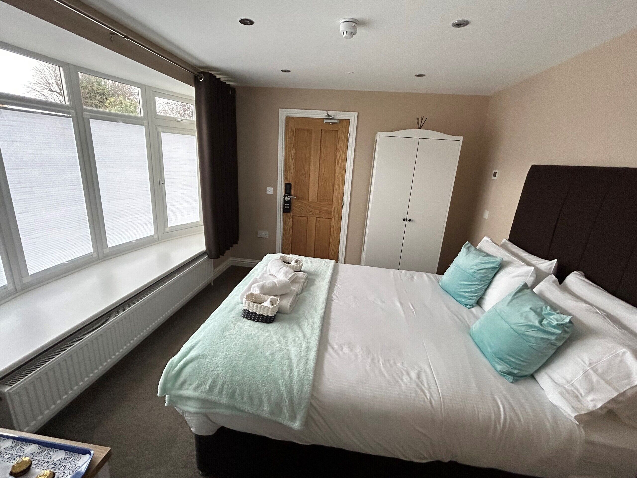A bedroom with a large bed, a wardrobe, a radiator, and a window with curtains.