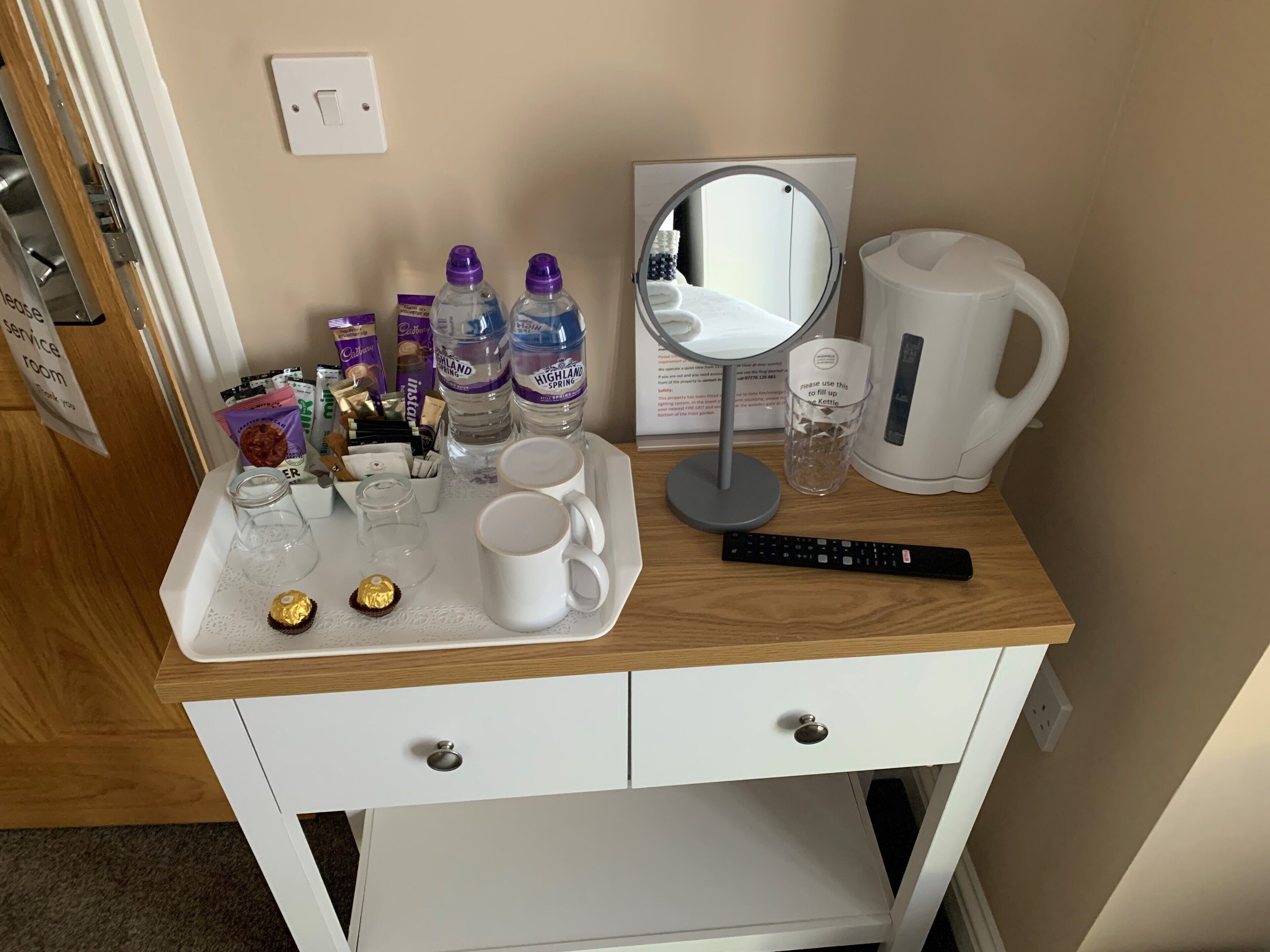 Escritorio de una habitación de hotel con una bandeja que contiene una cafetera, dos tazas, un control remoto y varios artículos de aseo.