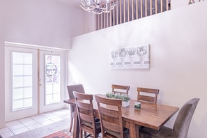 A dining area with a wooden table and chairs, a chandelier, and a wall-mounted artwork. - The Hen House Monthly Rental (Payson)