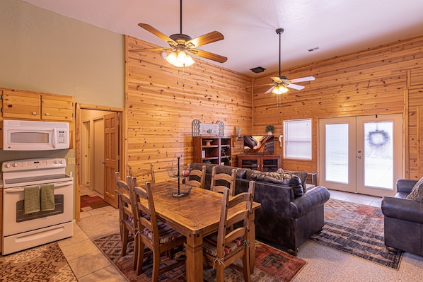 A cozy log cabin interior with a dining area, a fireplace, and a living room with a couch and a television.