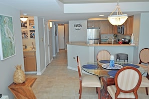 A modern kitchen with a dining area, featuring a glass-top table, wooden chairs, and a chandelier.