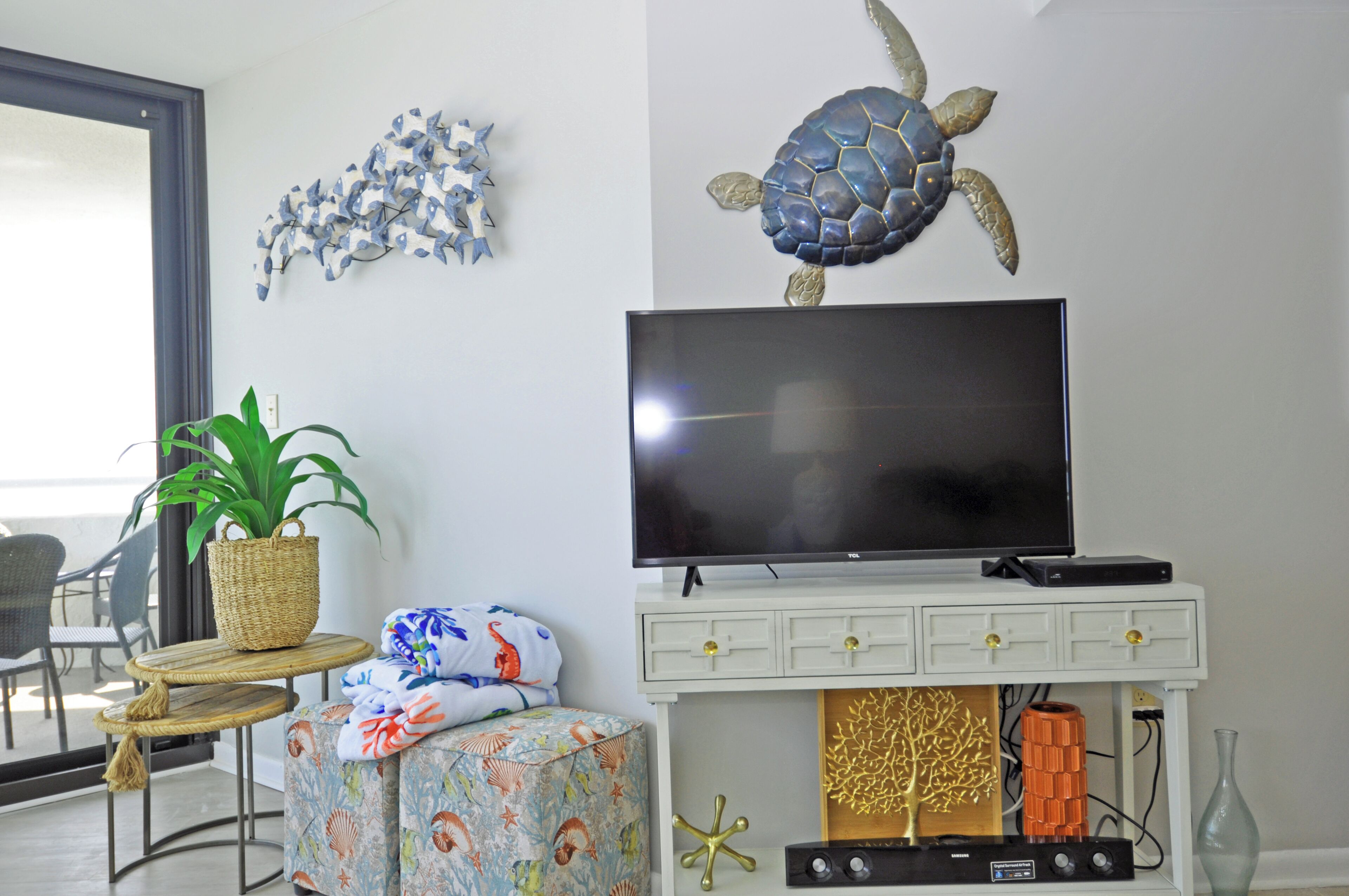 Ein Wohnzimmer mit Fernseher, einem Blumentopf, Wandkunst mit einer Schildkröte und einem kleinen Tisch mit Stuhl.