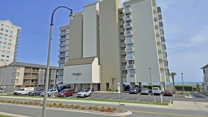 Een hoog hotel met meerdere balkons, een parkeerplaats en een helder uitzicht op het strand.