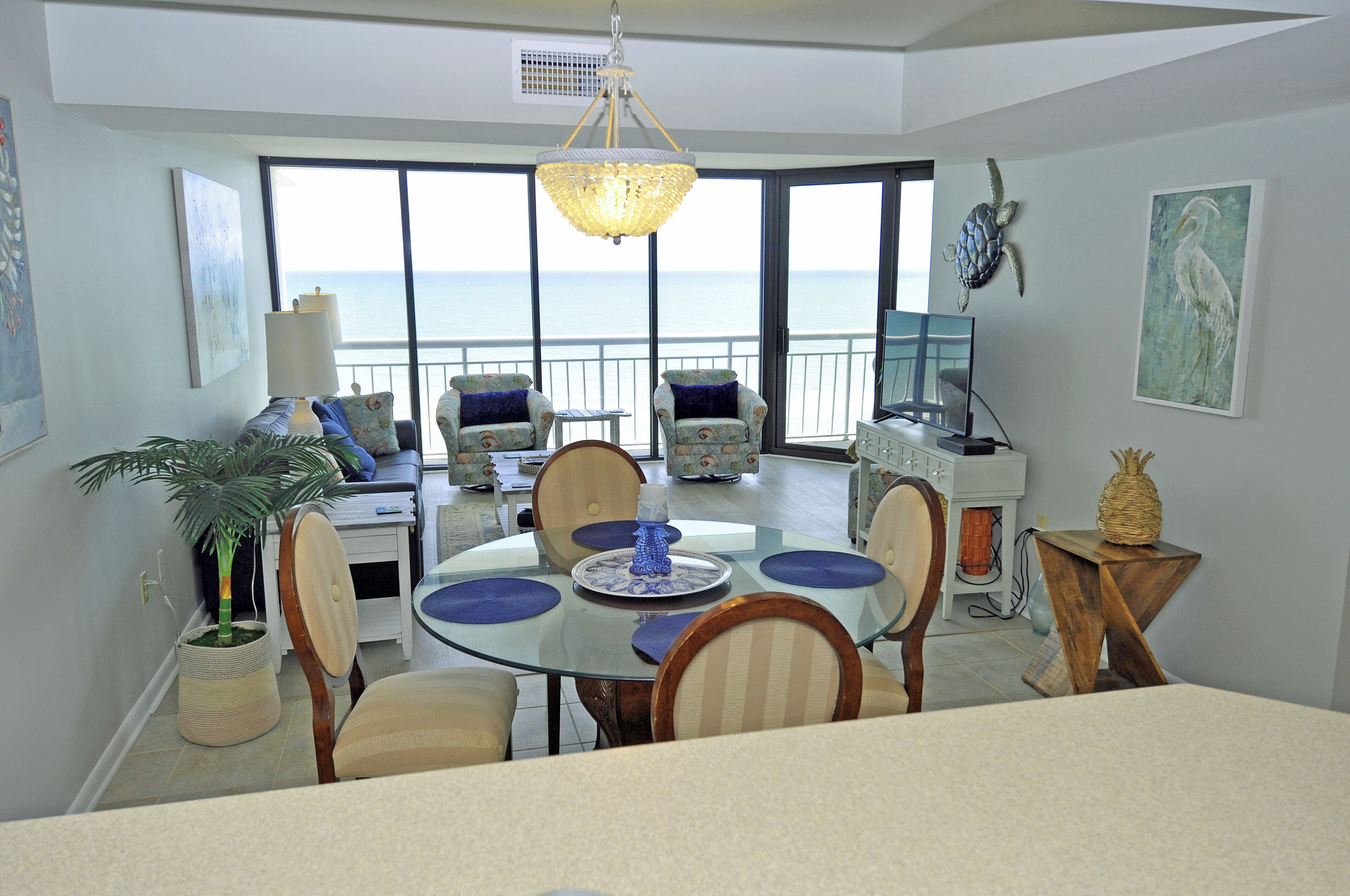 A dining area with a glass table, chairs, and a view of the ocean.