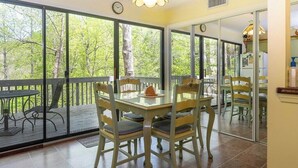 A dining area with a glass table and chairs, large windows, and a view of trees. - Fairway Villa 1101 at Rumbling Bald (Lake Lure)