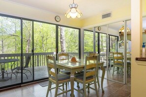A dining area with a glass table and chairs, large windows, and a view of trees.