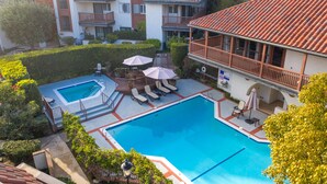 Una piscina con tumbonas y sombrillas, rodeada de un jardín cuidado y un edificio de varios pisos con balcones.