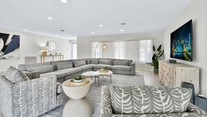 A modern living room with a sectional sofa, a coffee table, and a TV mounted on the wall. - 6341 Managed By Brampton Park (Fort Lauderdale)